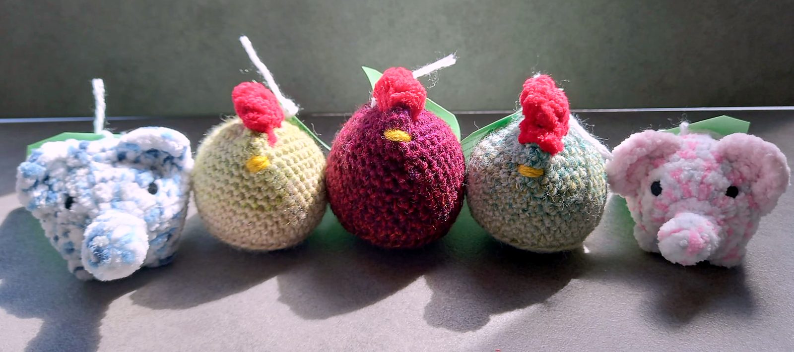 Round crocheted chickens with red combs between two little elephants