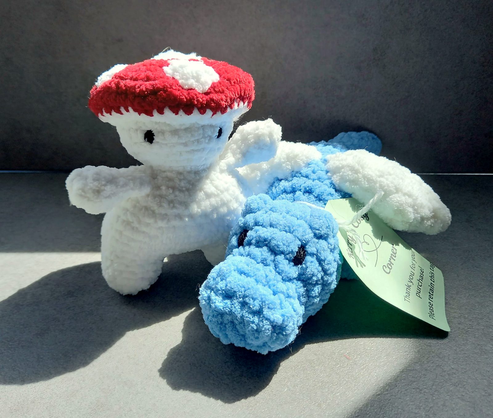 A crocheted mushroom friend with a red spotted cap next to a blue platypus